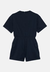 Μπλε ναυτικό κοντό συνολάκι με κοντά μανίκια, ελαστική μέση και δύο πλαϊνές τσέπες. Λείο υφασμάτινο σχέδιο με κλείσιμο στο πίσω μέρος. Μινιμαλιστικός σχεδιασμός.