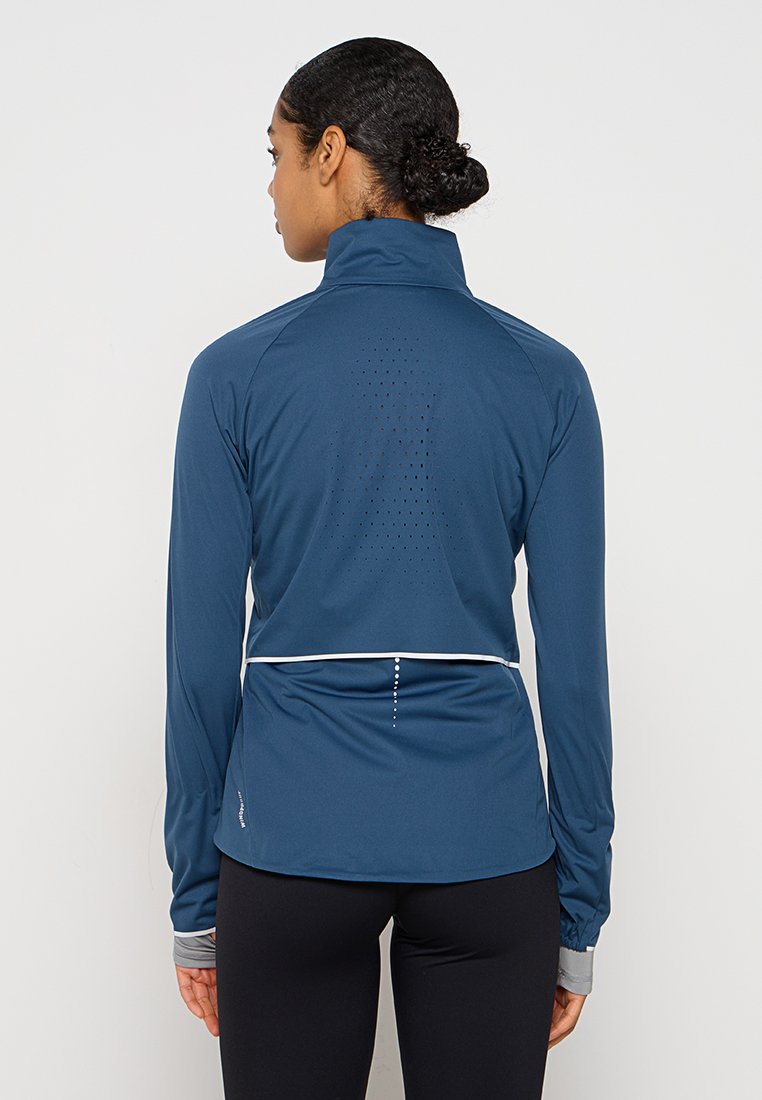 Marineblaue Sportjacke mit langen Ärmeln, hohem Kragen und reflektierenden Akzenten. Verfügt über atmungsaktive Mesh-Details auf dem Rücken und einem abgerundeten Saum.