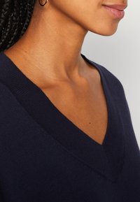 Pull en maille bleu marine à col en V avec un col côtelé et une texture douce, montrant un gros plan de la zone du col et du cou.