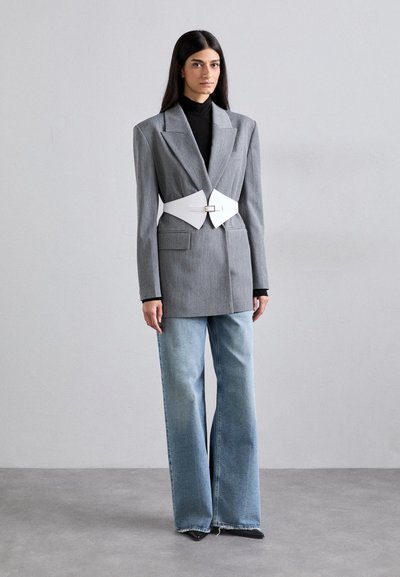 Hallhalline pinstriipe ülikond, millel on suurenenud õlg, koos valge vööd ja laia jalgadega helesiniste teksadega. Must turtleneck all.