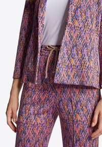 Wielokolorowy zestaw żakietu i spodni z geometrycznym wzorem w diamenty w kolorze różowym, niebieskim i pomarańczowym, o luźnym kroju i sznurkiem w talii.