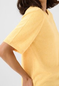 Maglione giallo a maniche corte in maglia con vestibilità comoda. Presenta un collo a V e polsini a costine. Texture morbida e delicato motivo melangiato.