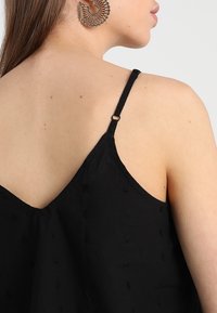 Black, lightweight camisole with thin straps and decorative textured dots. Back features a v-cut and metal hardware for strap adjustment.