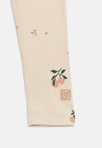 Κρεμ κολάν από ριμπ ύφασμα με μικρά μοτίβα ροδάκινου και φύλλων και τετράγωνο λογότυπο κοντά στο τελείωμα σε λευκό φόντο.