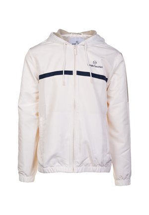 Chaqueta blanca con cremallera y capucha, con rayas horizontales azul marino en el pecho y puños elásticos. Fabricada con tejido ligero.