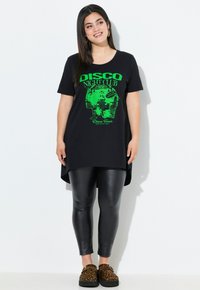 Black oversized t-shirt with green disco-themed graphic, paired with black shiny leggings and leopard print slip-on shoes.