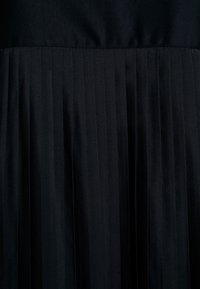 Tissu d'une robe noire plissée, avec une partie supérieure lisse et un bas texturé plissé. Texture douce, couleur uniforme. Pas de motifs ou d'accents visibles.