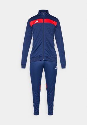 Tamsiai mėlynas treningas su raudonomis detalėmis. Jaketo ypatybės - aukštas apykaklė ir užtrauktukas. Kelnės turi šonines juosteles ir logotipą, pagamintos iš kvėpuojančios medžiagos.