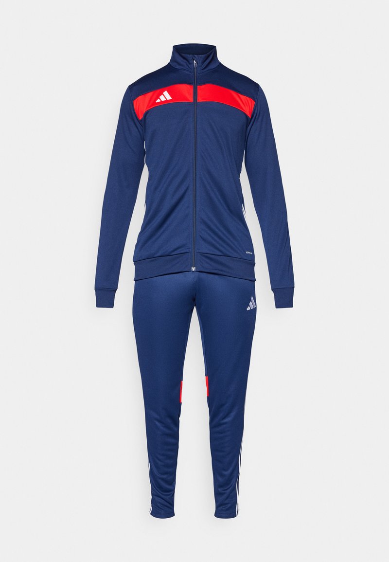 Chándal navy con acentos rojos. La chaqueta tiene un cuello alto y cierre de cremallera. Los pantalones cuentan con franjas laterales y un logo, fabricados en tejido transpirable.