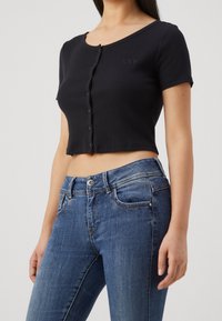 Svart ribbad kortärmad t-shirt med knäppning framtill och en liten logotyp. Matchad med blå denimjeans med en figursydd design.