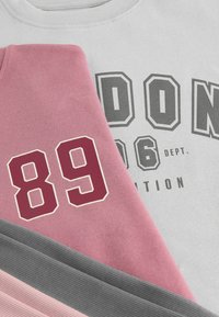 Harmaat, vaaleanpunaiset ja tummanharmaat collegepaidat pinottuina. Harmaassa paidassa on rohkea teksti "LONDON", vaaleanpunaisessa paidassa on luku "89" marooninvärisenä, molemmissa on sileä rakenne.