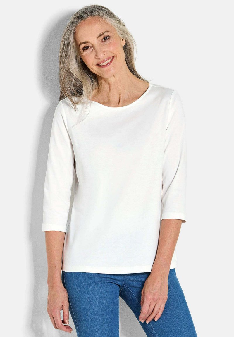 Witte lange mouwen top met een ronde halslijn en driekwartmouwen, gecombineerd met blauwe denim jeans. Gladde textuur, casual ontwerp.