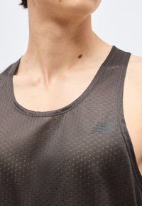 Κοντινό πλάνο ενός ατόμου που φοράει σκούρο γκρι αθλητικό τοπ χωρίς μανίκια με διακριτικό υφασμάτινο μοτίβο και μικρό λογότυπο στο στήθος.