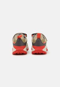 Zapatillas deportivas con una parte superior de malla transpirable en beige, acentuadas con detalles en goma gris y roja, que presentan una suela texturizada para un mejor agarre.