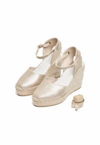 Espadrilles compensées en métal doré avec orteils ronds et brides de cheville, présentant des semelles en jute tressé et des enveloppements de talon beige plat.
