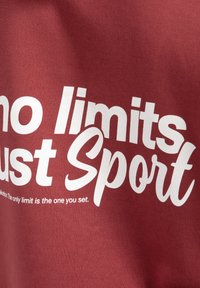 Czerwona bawełniana koszulka z dużym białym napisem: "bez ograniczeń tylko Sport" z mniejszym hasłem poniżej. Miękka tekstura, luźny krój.