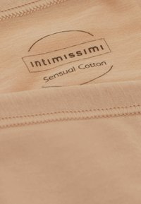 Perzikkleurige katoenstof met een gladde textuur. Bevat een label met "Intimissimi" en "Sensual Cotton" in het zwart gedrukt.
