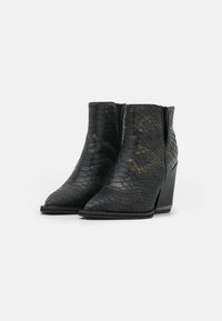 Botas negras hasta el tobillo hechas de cuero texturizado con un patrón de piel de serpiente, puntera afilada y tacón cuña. Acabado liso con costuras verticales.