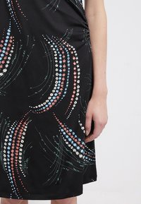 Robe noire avec un motif floral en rouge, bleu et blanc. Dotée de détails froncés sur les côtés et d'une texture lisse. Courte, coupe ajustée.