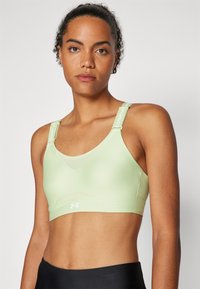 Sujeción deportiva verde claro con una textura suave, tirantes ajustables que presentan una marca blanca y un sutil detalle de malla en la parte delantera.