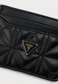 Μαύρο δερμάτινο πορτοφόλι για κάρτες με καπιτονέ σχέδιο, χαραγμένα γράμματα "G" και τριγωνικό σήμα λογότυπο Guess USA στο κέντρο.