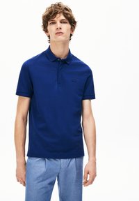 Marineblauwe polo met een kraag, korte mouwen en een subtiele logo op de borst, gecombineerd met lichtblauwe broeken.