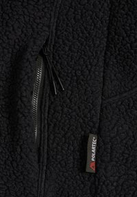 Schwarzer, strukturierter Fleece-Stoff mit einem schwarzen Reißverschluss und einem schwarzen Etikett mit der Aufschrift "Polartec" in weißen und roten Buchstaben.
