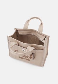 Sac cabas en toile beige avec poignées courtes, poche avant, ouverture zippée, et "Coach New York" brodé en marron.