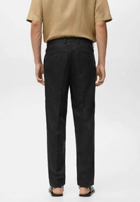 Pantaloni neri realizzati in un tessuto liscio, con una vestibilità dritta, tasche posteriori e una vita. Indossati con una camicia corta beige.