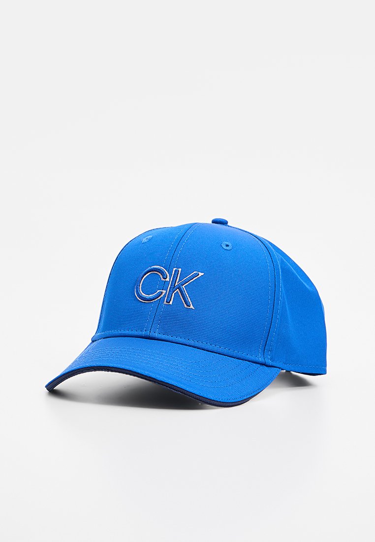 Blauwe stoffen baseballpet met een verhoogd "CK" logo in lichtblauw, voorzien van een gebogen rand en gestikt detail langs de randen.