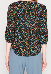 Blouse noire à motifs floraux avec des fleurs multicolores, des manches bouffantes, un ourlet arrondi et un tissu léger.