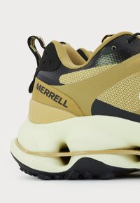 Zapatillas deportivas con una parte superior de malla negra y marrón, acentos texturizados, una suela acolchada de color crema y el logotipo de Merrell visible en el talón.