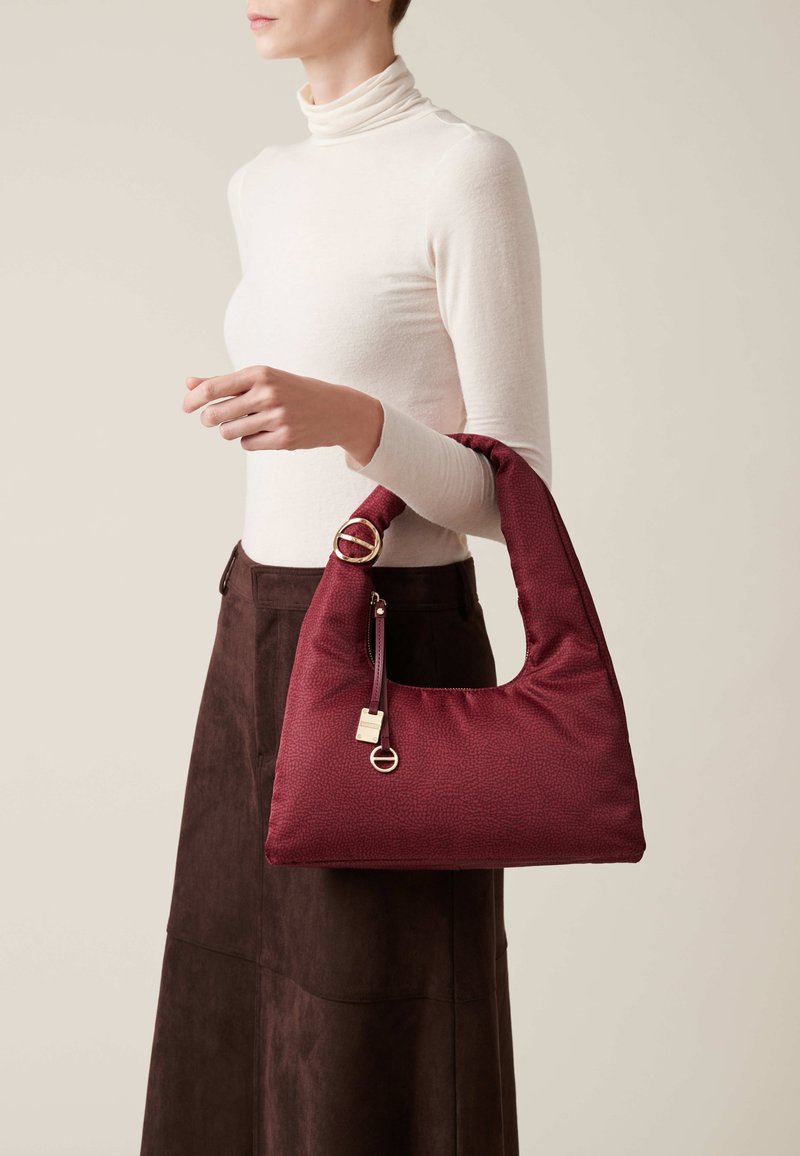 Burgundy handbag with a soft texture, slouchy design, and rounded handle, featuring gold hardware and a zippered pocket detail.