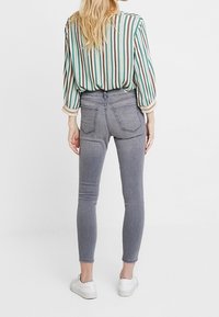 Jeans de mezclilla gris ajustados con cintura alta, bolsillos traseros y un ligero estiramiento, combinados con una camisa a rayas multicolor y zapatillas blancas.