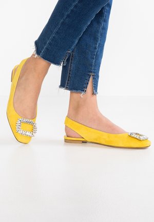 Gule ruskinds slingback flade med en firkantet spænde prydet med rhinsten. Flad hæl, glat tekstur og spids tå design.