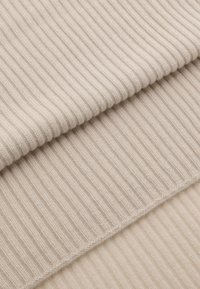 Beige ribbet strikstof, blød tekstur, to synlige lag, hver med distinkte vandrette striber, ensartet mønster overalt.