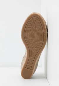 Suela de un zapato tejido en color beige con una parte inferior de goma texturizada y la marca "Tommy Hilfiger" en el área del arco.