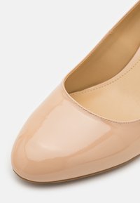 Chaussure plate pour femme en cuir verni beige brillant, avec bout arrondi et doublure cousue à l'intérieur, photographiée sur fond blanc.