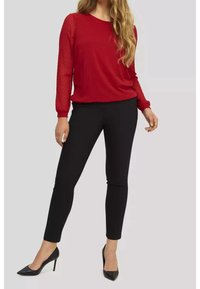 Haut rouge à manches longues avec texture à points et col rond, associé à un pantalon noir ajusté et des talons noirs pointus. Design et coupe simples.