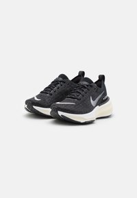 Baskets de sport noires avec une tige en tricot texturé, logo Nike blanc, et un col rembourré. Présentent une semelle intermédiaire blanche et une semelle en caoutchouc.
