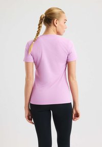 Rosa t-shirt med kort ärm, slät textur, figurnära passform och rundad halsringning, ihop med svarta leggings. Synligt flätat hår.