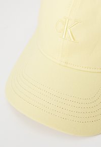 Gele stoffen pet, voorzien van een geborduurd "CK" logo, een gebogen klep en een gestikte textuur. Eenvoudig en strak ontwerp.