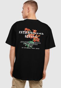 Juodas didelis t-shirt'as su spalvingais gėlių grafikos raštais ir tekstu ant nugaros, su laisvu siluetu ir apvalia iškirpte.
