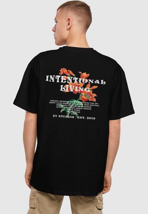 Sort oversized t-shirt med farverige blomstergraphics og tekst på ryggen, med en afslappet pasform og rund halsudskæring.