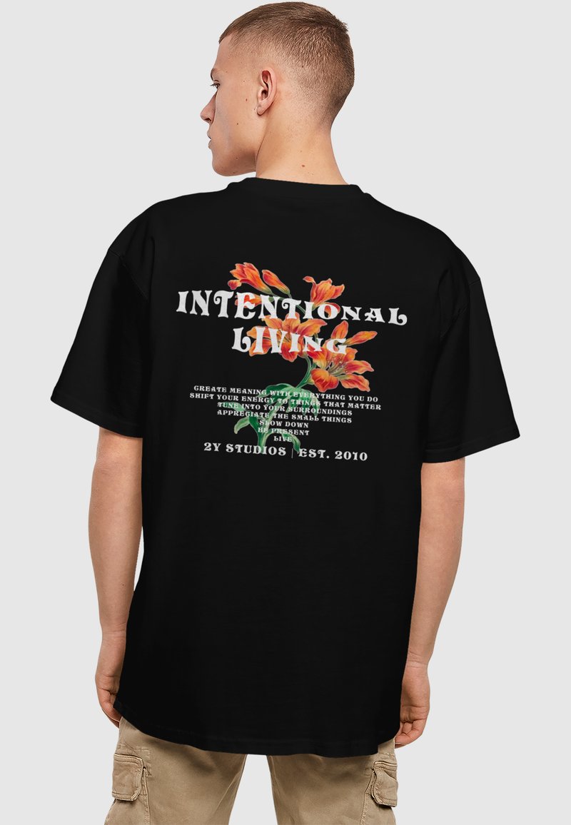 Juodas didelis t-shirt'as su spalvingais gėlių grafikos raštais ir tekstu ant nugaros, su laisvu siluetu ir apvalia iškirpte.
