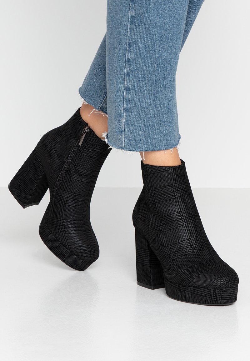 Bottines noires en matériau synthétique texturé, présentant un motif à carreaux, un talon bloc haut et une fermeture éclair latérale.