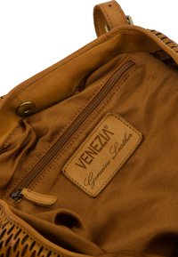 Interieur van een bruin leren handtas met een ritszak en een "VENEZIA Echt Leer" label. Glad textuur met gestikte accenten.