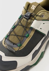 Outdoor shoe featuring a mesh upper in olive and gray, textured accents, elastic laces, and a contrasting white and dark sole.