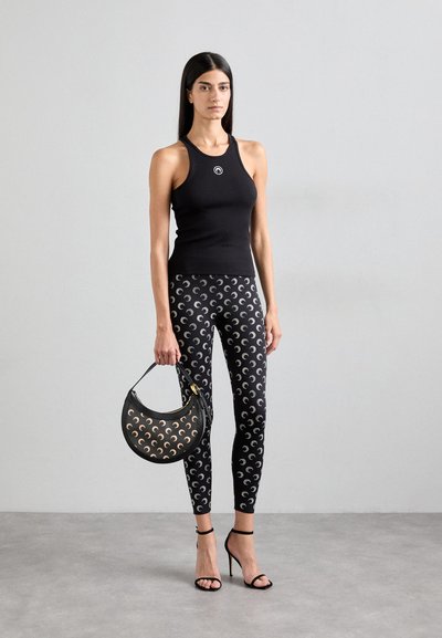 Top sin mangas negro con un logo circular, leggings negros con un patrón de formas de media luna y una bolsa negra con diseño troquelado.
