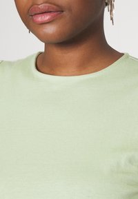 Camiseta de manga corta de color verde claro, con cuello redondo, hecha de una tela suave, que presenta una textura lisa y costuras mínimas.